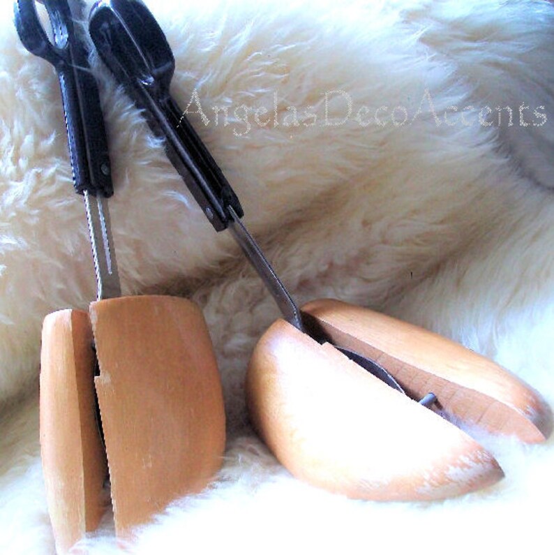 K&ouml;nnte beinhalten: Zwei Schuhspanner aus Holz mit schwarzen Griffen und Metallkomponenten. Die Schuhspanner sind hellbraun und dienen dazu, die Form und Gr&ouml;&szlig;e der Schuhe zu erhalten. Der Hintergrund ist eine flauschige, wei&szlig;e Oberfl&auml;che.