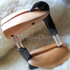 K&ouml;nnte beinhalten: Ein Schuhspanner aus Holz mit schwarzen Kunststoff- und Metallkomponenten. Die Schuhform ist hellbraun, mit einem geschwungenen Design. Der Spanner dient dazu, die Form der Schuhe zu erhalten und Falten zu vermeiden. Der Text "AngelasDecoAccents" ist sichtbar.