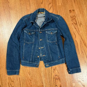 May include: A classic blue denim jacket with a button-up front, two chest pockets, and two side pockets. The jacket has a collared neckline and long sleeves. The denim is a medium wash, and the jacket appears to be in good condition.