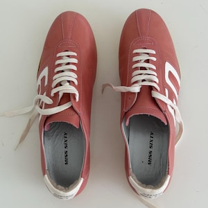May include: Pair of pink leather sneakers with white laces and accents. The sneakers have the words "MISS SIXTY" printed on the insole and a white design on the side. The shoes are new.