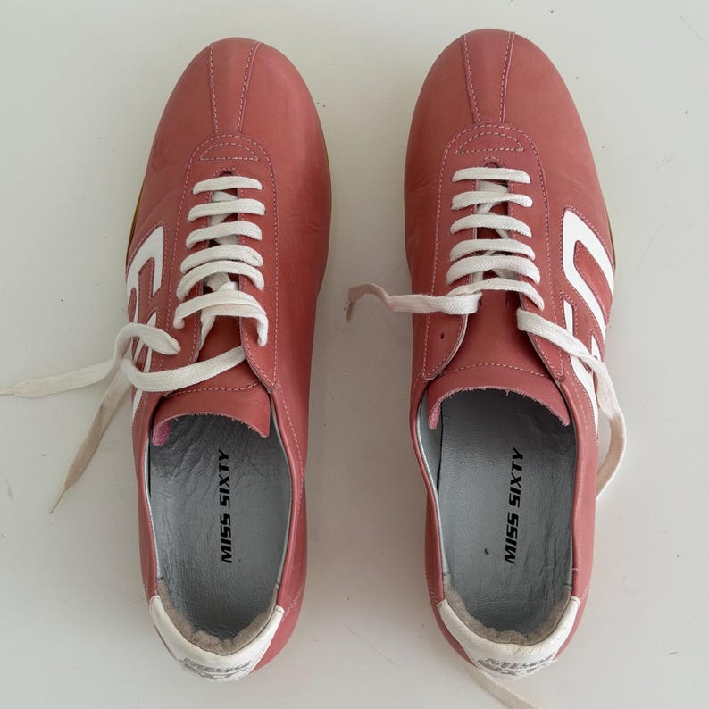 May include: Pair of pink leather sneakers with white laces and accents. The sneakers have the words "MISS SIXTY" printed on the insole and a white design on the side. The shoes are new.
