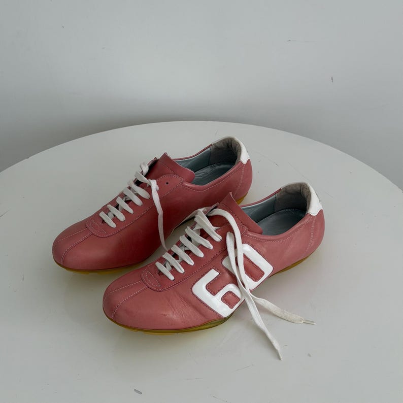 May include: A pair of pink sneakers with white laces and accents. The shoes have a retro design with the number "60" in white on the side. The soles are yellow.