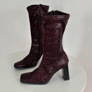 Może przedstawiać: Para burgundowych skórzanych kozaków z kwadratowym noskiem i grubym obcasem.