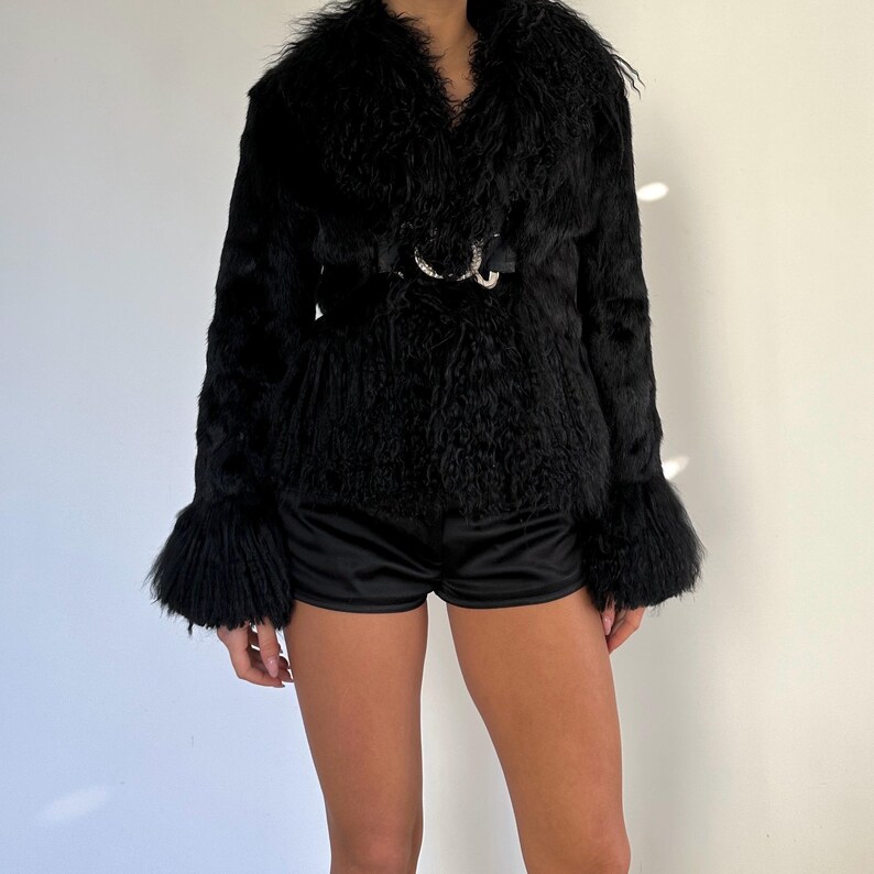 Peut inclure: Veste noire en fausse fourrure avec un large col et une ceinture &agrave; boucle d&eacute;corative. La veste a des manches longues avec des poignets &eacute;vas&eacute;s. Le mod&egrave;le porte un short en satin noir.