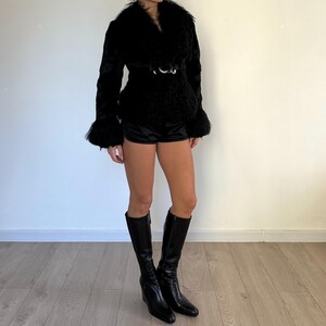 Peut inclure: Veste noire en fausse fourrure avec un large col et des manches &eacute;vas&eacute;es. La veste est cintr&eacute;e &agrave; la taille par une ceinture &agrave; boucle argent&eacute;e. La tenue comprend un short noir et des bottes noires montantes.