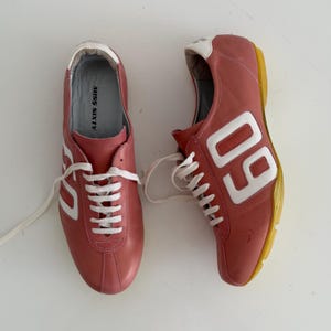 May include: Pair of pink leather sneakers with white laces and accents. The sneakers feature the number "60" in white on the side and the text "MISS SIXTY" on the insole. The soles are yellow.