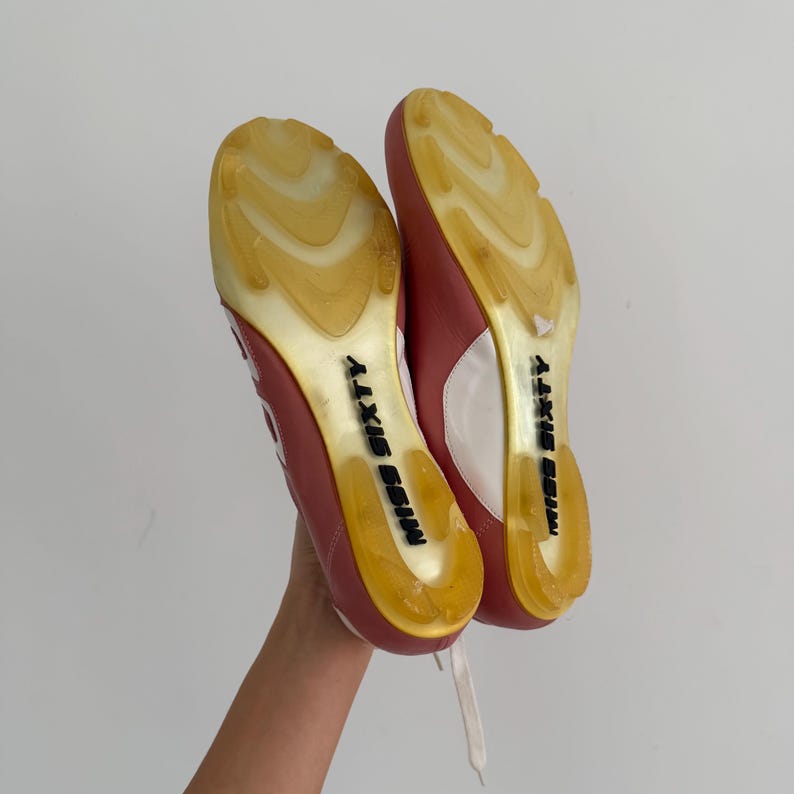 May include: A pair of red and white sneakers with a clear yellow sole. The soles have the words "MISS SIXTY" printed in black. The sneakers are held up by a hand.