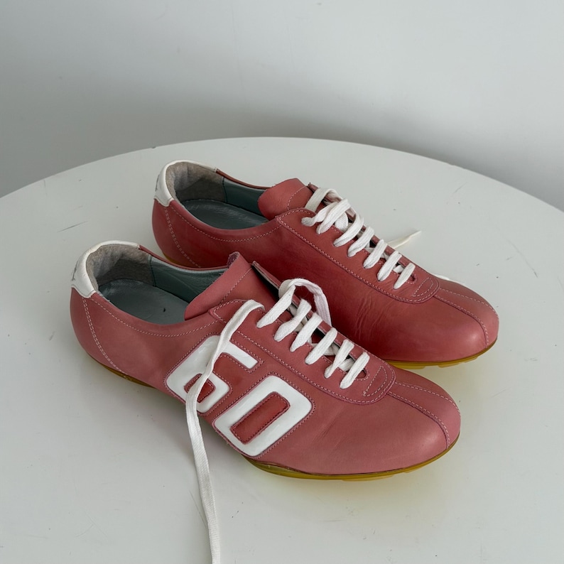 May include: A pair of pink leather sneakers with white laces and accents. The sneakers have a retro design with the number "60" in white on the side. The soles are yellow.