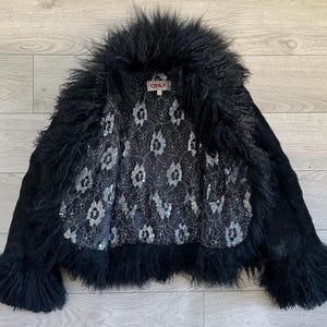 Peut inclure: Veste noire avec un col et des poignets en fourrure hirsute. La veste a un ext&eacute;rieur noir et une doublure int&eacute;rieure &agrave; motifs. L'&eacute;tiquette "ONLY" est visible. La veste est ouverte, r&eacute;v&eacute;lant la doublure.