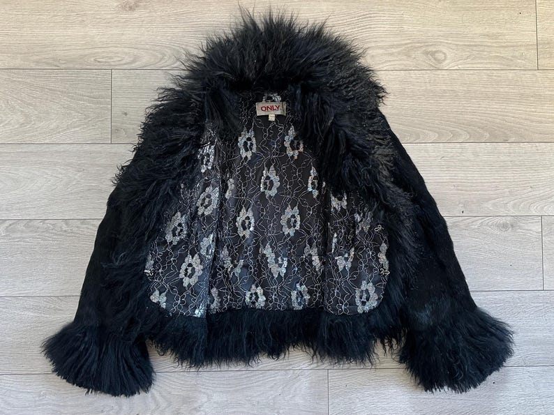 Peut inclure: Veste noire avec un col et des poignets en fourrure hirsute. La veste a un ext&eacute;rieur noir et une doublure int&eacute;rieure &agrave; motifs. L'&eacute;tiquette "ONLY" est visible. La veste est ouverte, r&eacute;v&eacute;lant la doublure.