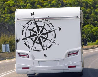 May include: A white camper van with a black compass sticker on the back. The compass has the letters N, S, E, and W around the outside.