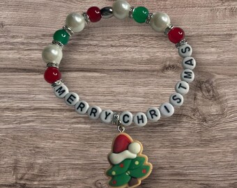 May include: White beaded bracelet with red and green beads, spelling out "Merry Christmas" with a charm of a Christmas tree with a Santa hat.