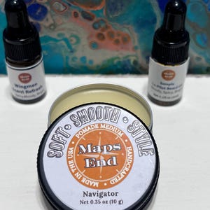 May include: A black tin of pomade with the text "Maps End Navigator" and two small dropper bottles. The tin is labeled "Soft Smooth Style Pomade Medium" and contains 10 g. The bottles are labeled "Wingman Scent Refresh" and "Sample Co-Pilot Beard Oil".