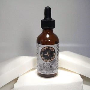 May include: A brown glass bottle of Maps End Co-Pilot Beard Oil with a black dropper. The label features a compass rose design and the text "Woody, Spicy, Bright." The bottle contains 2 fl oz (56ml) of product.