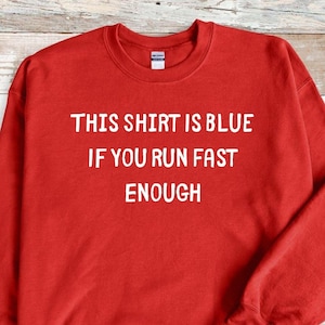 Könnte beinhalten: Roter Pullover mit dem Text "This shirt is blue if you run fast enough" in Weiß.