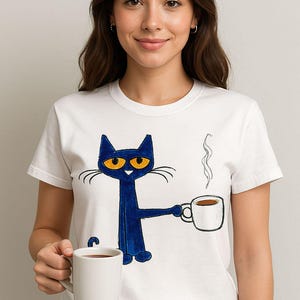 May include: White t-shirt with a blue cat holding a white coffee mug. The cat has orange eyes and a white mustache. The cat is wearing a blue shirt. The text on the shirt says "Blue's Clues".