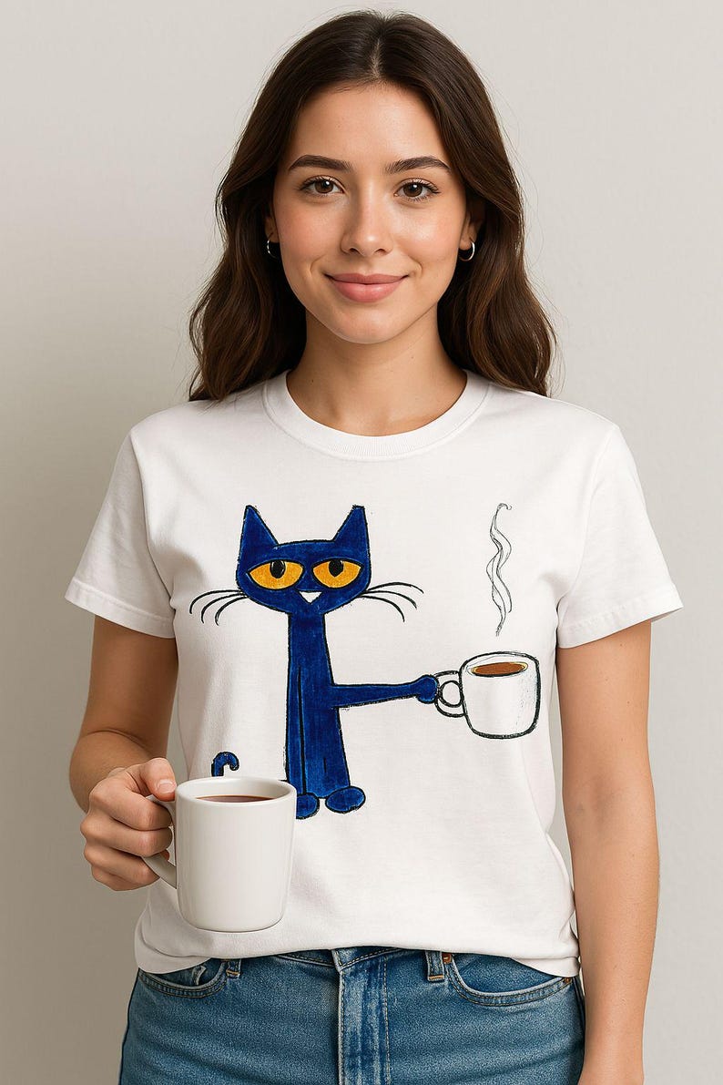 May include: White t-shirt with a blue cat holding a white coffee mug. The cat has orange eyes and a white mustache. The cat is wearing a blue shirt. The text on the shirt says "Blue's Clues".