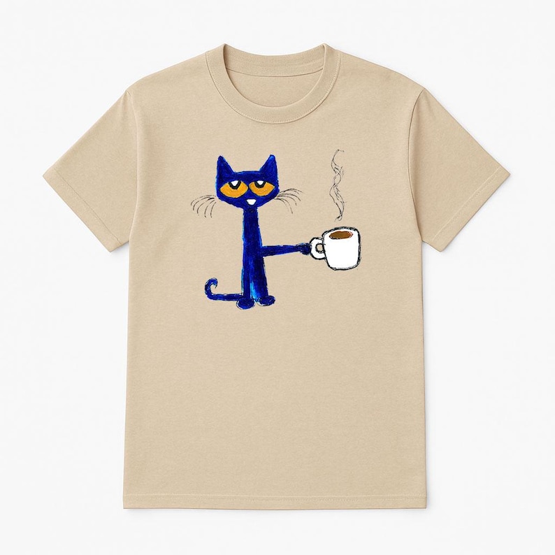 May include: A tan t-shirt with a blue cat holding a white coffee cup with a brown liquid inside. The cat has orange eyes and a black nose. The cat is drawn in a simple, childlike style.