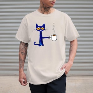 May include: A light beige t-shirt with a blue cat cartoon illustration holding a cup of coffee. The cat has large blue eyes and a white mustache. The text "I love you" is written above the cat.