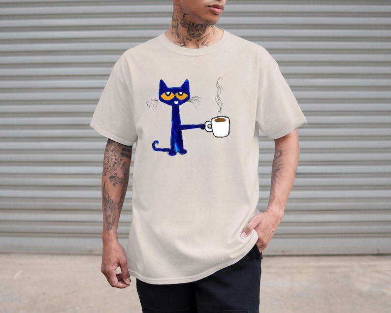 May include: A light beige t-shirt with a blue cat cartoon illustration holding a cup of coffee. The cat has large blue eyes and a white mustache. The text "I love you" is written above the cat.