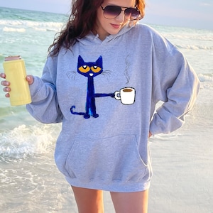 May include: A gray hoodie with a blue cat holding a cup of coffee. The cat has orange eyes and a white mustache. The text "Coffee" is written on the cup.