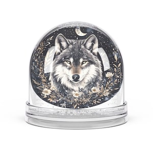 May include: A snow globe featuring a detailed illustration of a wolf's face. The wolf is surrounded by floral elements and set against a dark night sky with a crescent moon and stars. The base is clear.