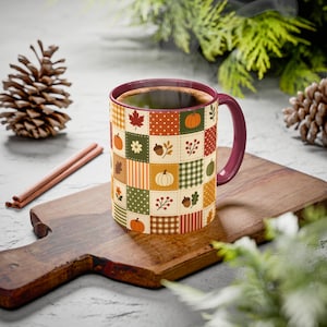 Peut inclure: Une tasse en céramique avec un intérieur et une anse bordeaux, ornée d'un motif patchwork de carrés sur le thème de l'automne. Le design présente des illustrations de citrouilles, feuilles d'érable, glands, fleurs et baies dans des tons orange, vert et marron.