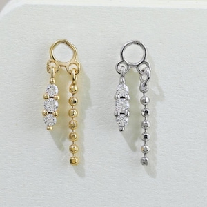 Könnte beinhalten: Ein Paar Ohrringe, einer goldfarben und einer silberfarben, jeweils mit einem kleinen Ring oben. Der goldfarbene Ohrring hat drei klare Steine und eine Kette aus kleinen Perlen. Der silberfarbene Ohrring hat ein ähnliches Design.