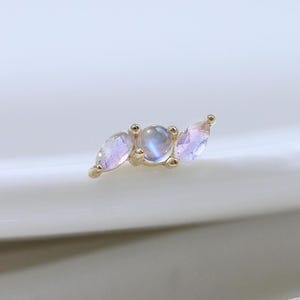 May include: A gold-toned earring featuring three iridescent moonstone gems. The central gem is round, flanked by two marquise-shaped stones. The earring is set against a white background, highlighting its delicate design.