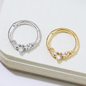 May include: Two decorative hoop earrings. One is silver-colored, the other is gold-colored. Both earrings feature a floral design with clear gemstones. The earrings are displayed on a white surface.