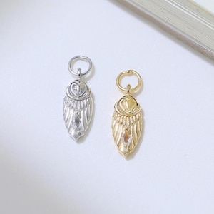 May include: Two small, metal owl charms. One is silver-colored, the other is gold-colored. Each charm has a loop at the top for hanging and a detailed owl design. The charms are on a white surface.