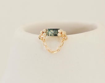 May include: A gold-colored earring with a rectangular, green gemstone at the top. The earring has a delicate chain design that hangs below the gemstone. The earring is set against a white background.
