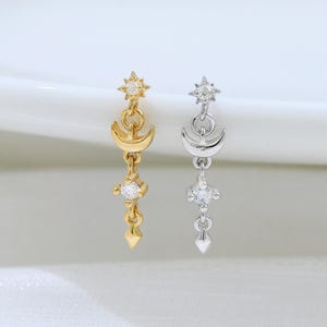 May include: Two dangle earrings, one in gold tone and one in silver tone, each featuring a small star at the top, a crescent moon shape, and a dangling clear stone accent at the bottom, suspended in a vertical line design with delicate metal links.