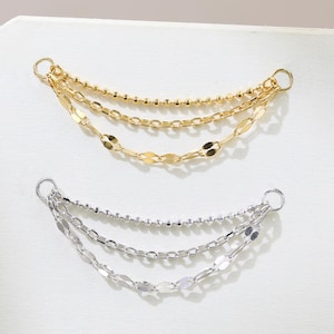 May include: Two sets of layered chain earrings. One set is gold-toned, featuring three chains with different textures: beaded, oval, and small round links. The other set is silver-toned, with similar chain styles. Both sets are displayed on a white surface.