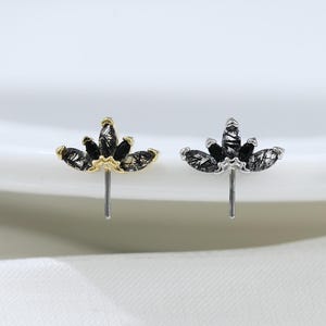 May include: Two stud earrings featuring a crown-like design with marquise-cut black rutilated quartz stones. One earring has a gold-tone metal setting, while the other has a silver-tone metal setting. Each piece includes a thin vertical post.