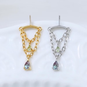 May include: A pair of earrings, one gold-toned and one silver-toned, each featuring a chain design. The gold earring has a green and a teardrop-shaped, multi-colored stone. The silver earring has a green and a teardrop-shaped, multi-colored stone.