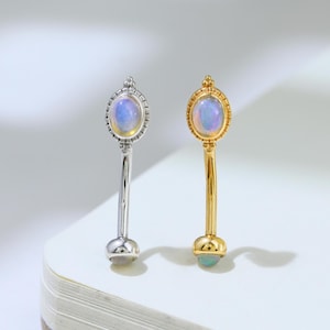 Peut inclure: Deux piercings de type barre courbe, l'un en métal argenté et l'autre en métal doré. Chacun présente une pierre ovale irisée semblable à une opale dans un cadre perlé au sommet et une petite pierre ronde assortie à l'extrémité inférieure.