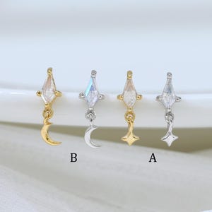 May include: Four stud earrings with celestial designs. Two are gold-toned with a diamond-shaped crystal and a dangling crescent moon or star. The other two are silver-toned with a diamond-shaped crystal and a dangling crescent moon or star.