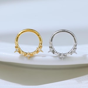 May include: Two circular hoop rings, one in gold tone and one in silver tone, each featuring a decorative celestial design with small star-shaped accents and clear stones embedded along the lower half of the circular band structure.