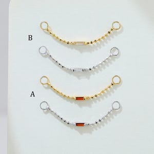 Puede incluir: Cuatro delicados collares de cadena con pequeñas cuentas redondas y piezas centrales rectangulares. Dos son dorados y dos plateados. Cada cadena tiene un pequeño lazo en ambos extremos. Los collares se muestran sobre una superficie blanca.