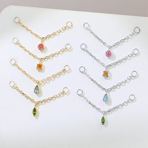 May include: Jewelry set featuring delicate chain designs in gold and silver. Each chain has a small, colorful gemstone pendant in various shapes and colors, including pink, orange, blue, and green. The jewelry is displayed on a white surface.