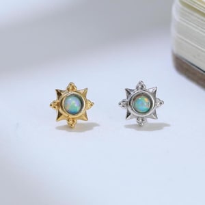 May include: Two stud earrings shaped like sunbursts, each featuring a central round iridescent opal cabochon. One earring is finished in a warm gold tone, while the other is finished in a cool silver tone, both displaying pointed rays.