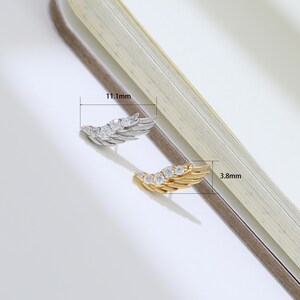 May include: Two wing-shaped earrings, one silver-toned and one gold-toned, each adorned with clear gemstones. The silver earring measures 0.44 inches in length, and the gold earring is 0.15 inches long. The earrings are displayed on a light-colored surface.