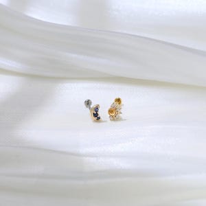 May include: Two gold body jewelry pieces, one with a crescent moon design with blue gemstones and the other with a sun design with clear gemstones.