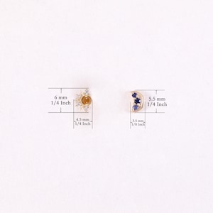 May include: A pair of gold earrings with a sun and moon design. The sun earring features a yellow gemstone surrounded by clear cubic zirconia stones. The moon earring features three blue sapphires. The earrings measure 6 mm (1/4 inch) and 5.5 mm (1/4 inch) in diameter.