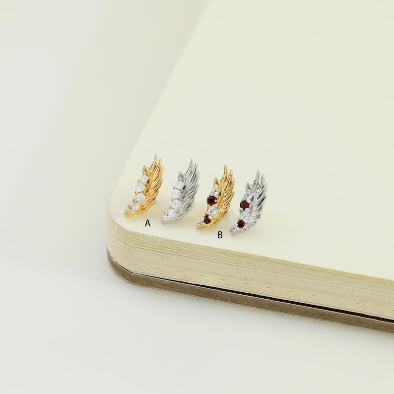 May include: Four feather-shaped earrings, each with a different design. Two are gold-toned, and two are silver-toned. Each earring has a row of small, clear gemstones. Two earrings have red gemstones. The earrings are labeled A and B.