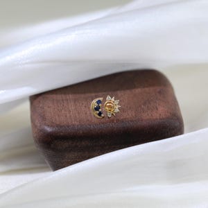 May include: A gold sun and moon earring with blue and white gemstones. The sun has a yellow center and the moon has a blue center.