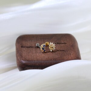 May include: Gold moon and sun cartilage earring with blue sapphire and citrine gemstones. The sun features a center citrine stone surrounded by smaller clear stones, labeled "Moissanite".