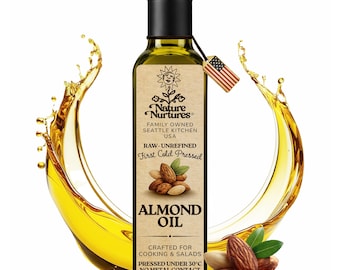May include: A clear glass bottle of almond oil with a black cap and a small American flag tag. The label reads "Nature Nurtures" and "Almond Oil". The bottle contains 250 ml. A splash of oil surrounds the bottle, with almonds in the foreground.