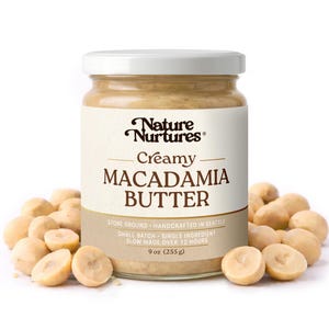 May include: A jar of creamy macadamia butter with the brand name "Nature Nurtures" on the label. The label also states "Creamy Macadamia Butter" and "9 oz (255 g)". Macadamia nuts surround the jar.